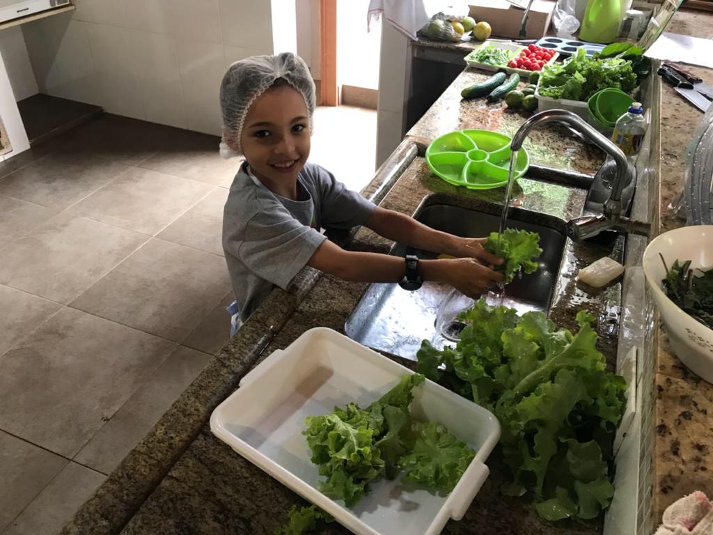 Criança higienizando folhas na cozinha